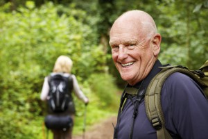 Senior man smiles back towards the camera while hiking with his wife in the forest. Horizontal shot.